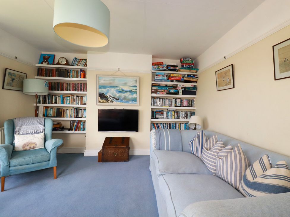 A living room with a sofa, bookshelf, and television at Chy-an-Lowena in Crantock
