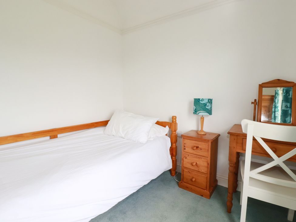 A bedroom with a bed, table, lamp, chair and mirror at Chy-an-Lowena in Crantock