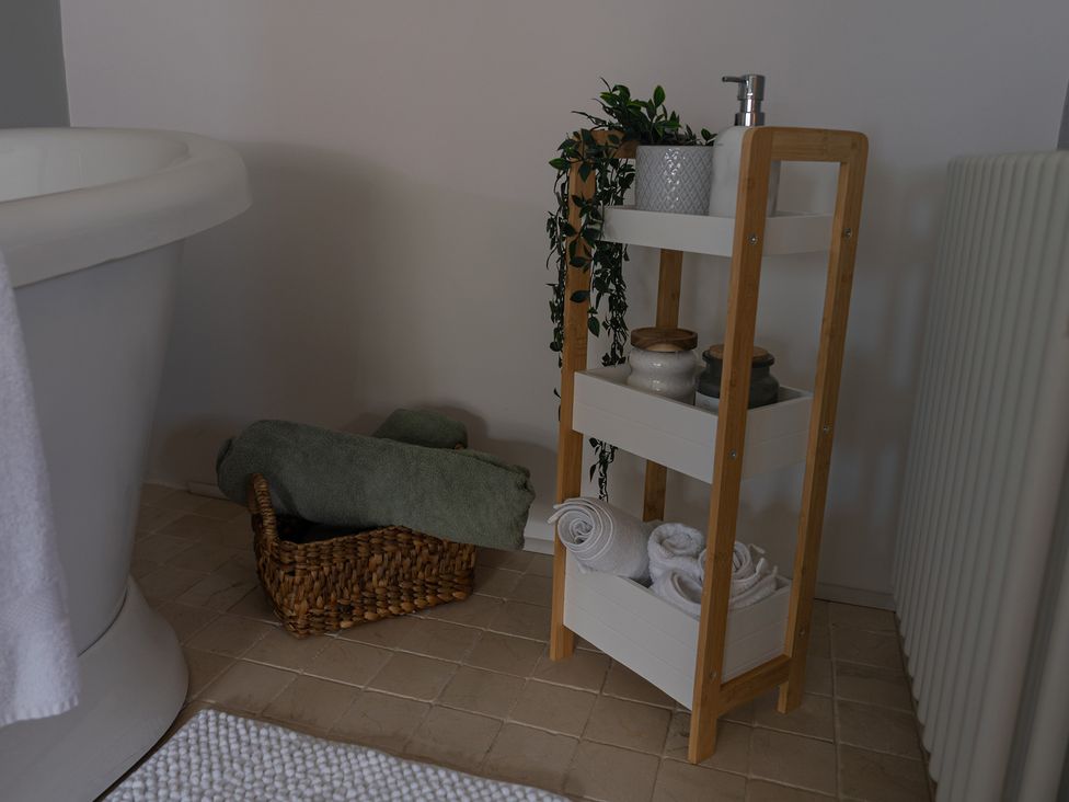 A bathroom with a bathtub, towels, and a shelving unit at The Old Print House in Stanley Common