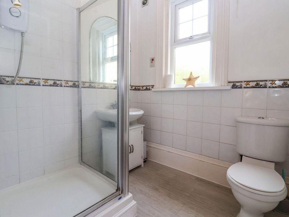 A bathroom with a shower, toilet, sink, and window at Trinity Lodge in Bridlington