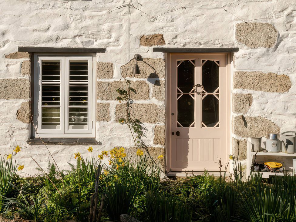 A pink door and a window on a stone wall at Rose Cottage in Gweek