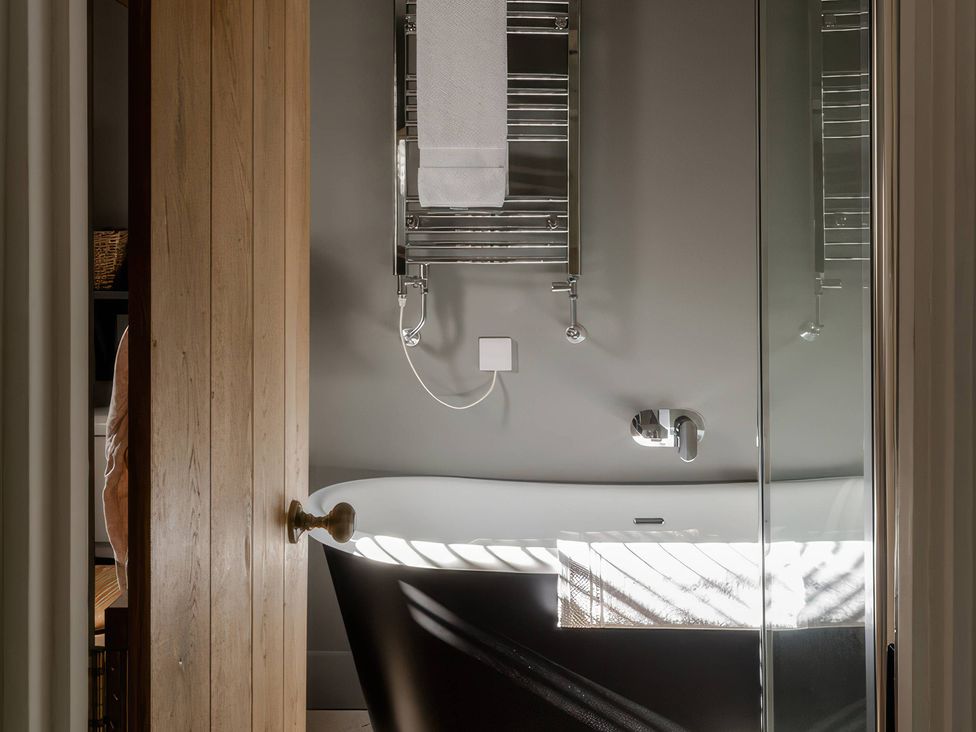 A bathroom with a bathtub and towel rail at Rose Cottage in Gweek
