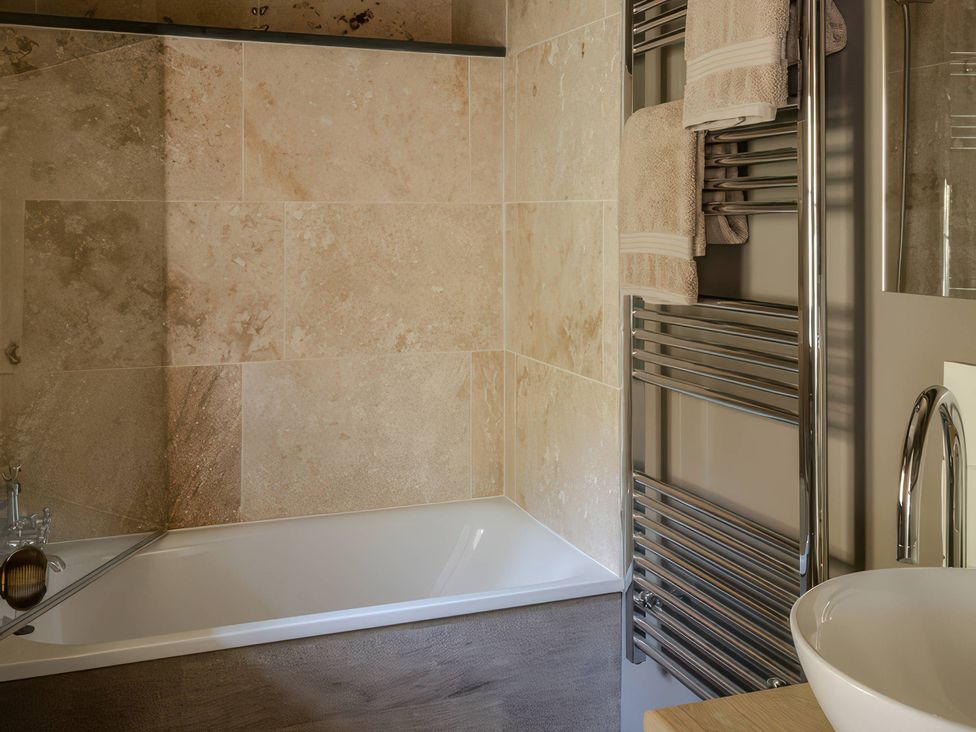 A bathroom with a bathtub and towel rack at Rose Cottage in Gweek