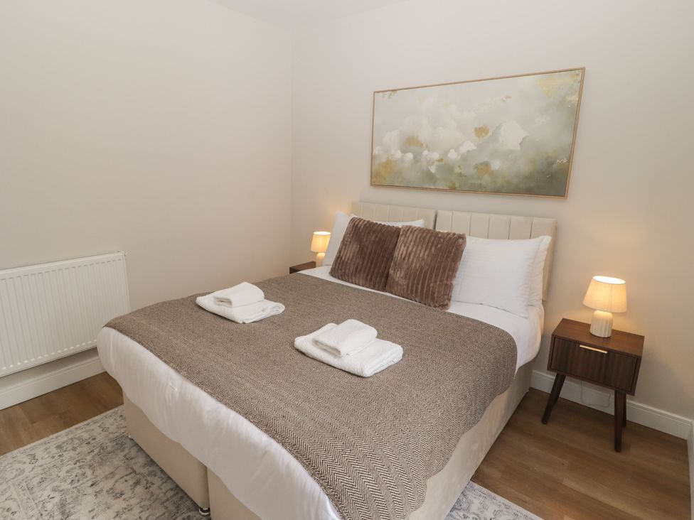 A bedroom with a bed, blanket, towels, lamp and radiator at Flat 1 in Tenby