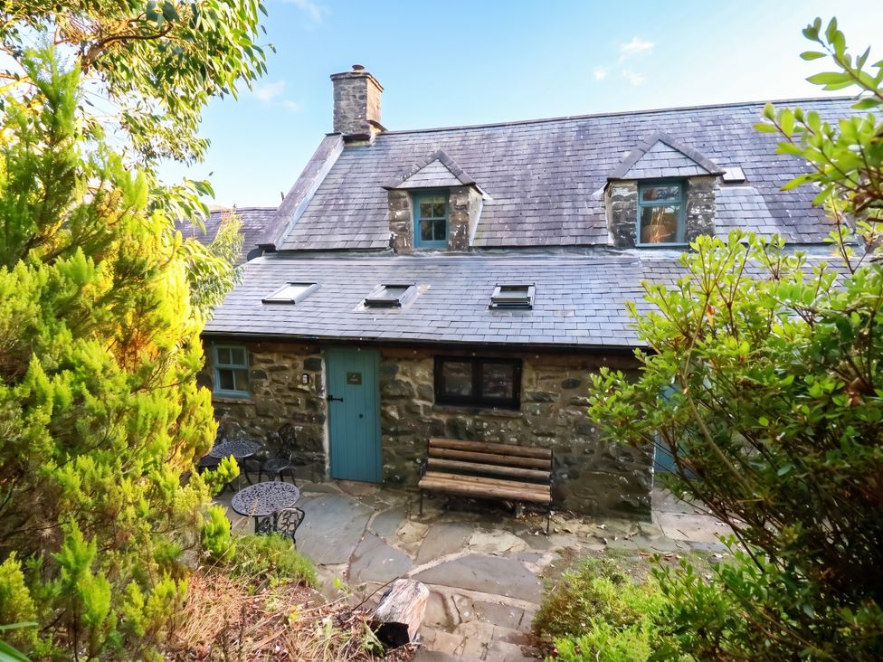 A cottage with a bench and table surrounded by greenery at Y Cwtch in Dolgellau