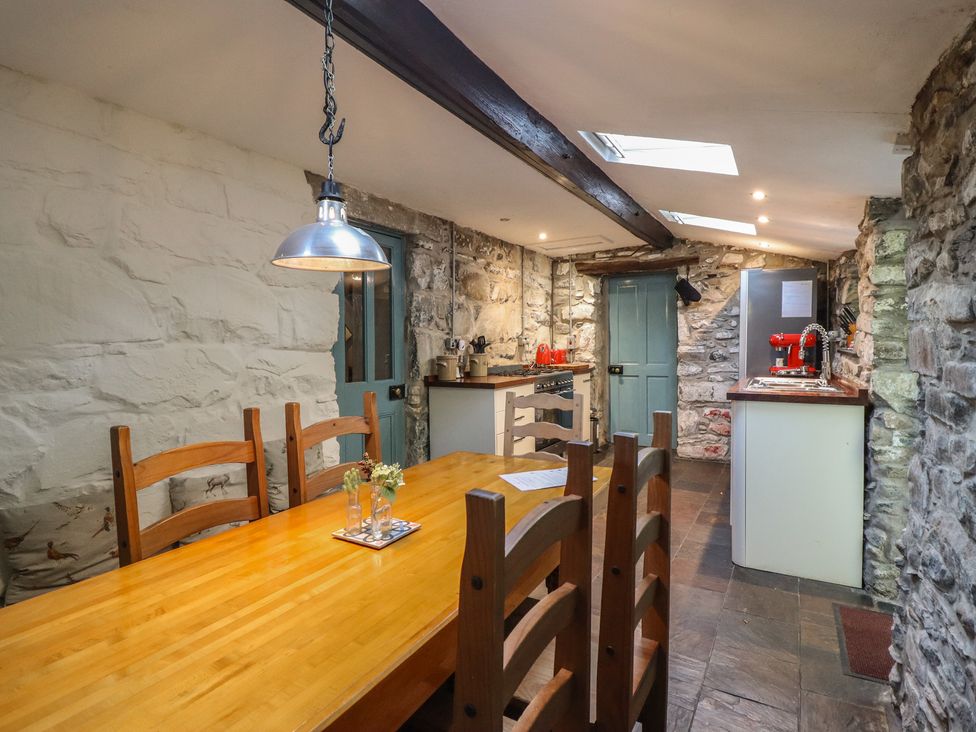 A kitchen with a dining area featuring a wooden table and stone walls at Y Cwtch in Dolgellau