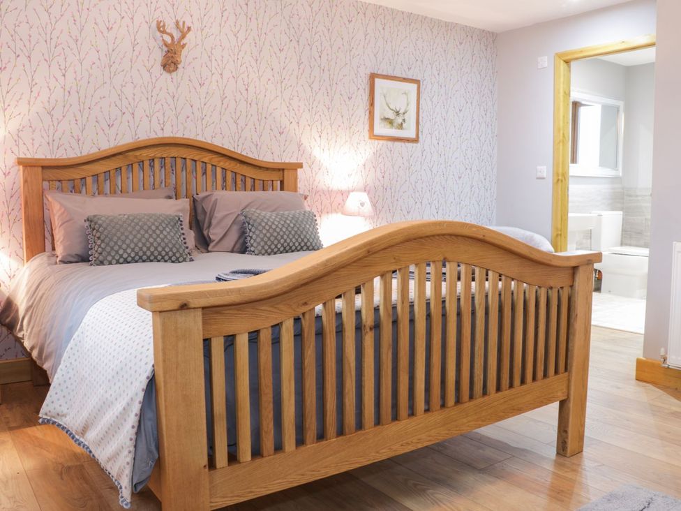 A bedroom with a wooden bed and bathroom access at Gardener's Lodge in Nantwich