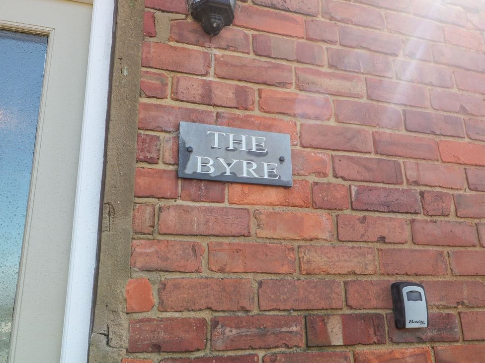 A nameplate mounted on a brick wall at The Byre in Ashbourne