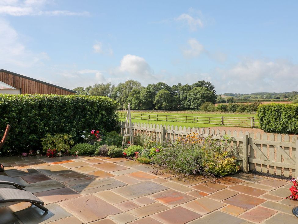 A garden with flowers, patio stones, and a fence at The Byre in Ashbourne