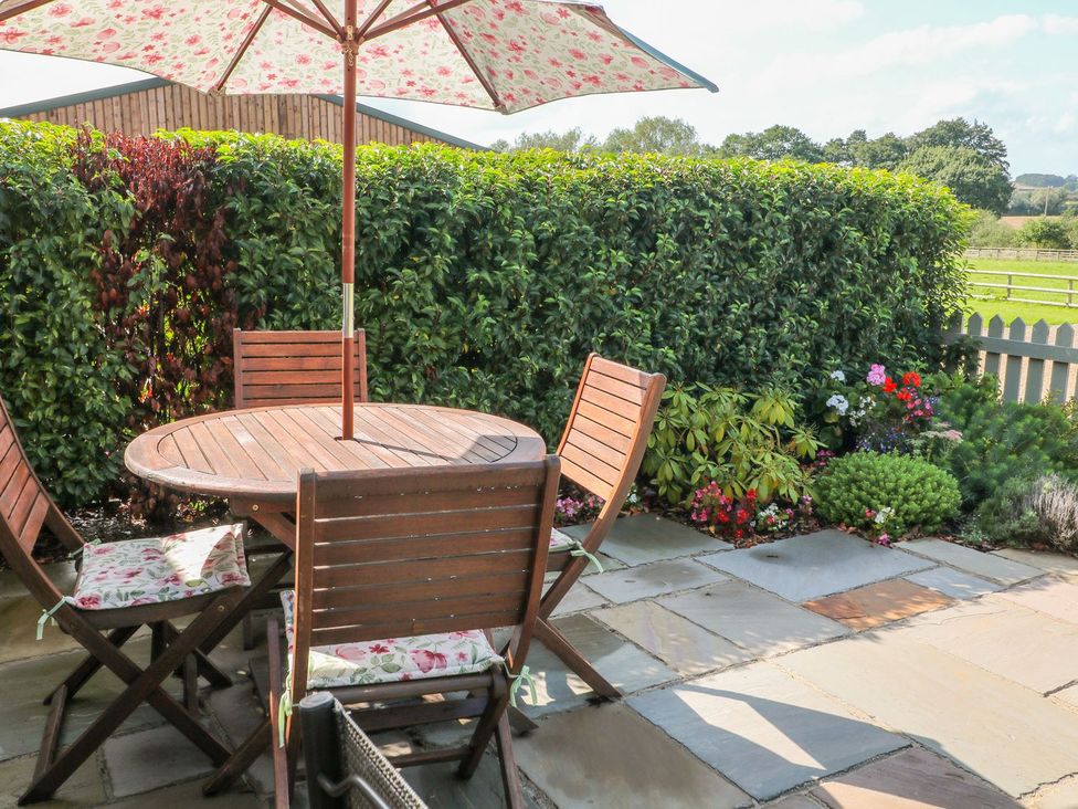 A garden area with a wooden table and chairs under an umbrella at The Croft in Ashbourne