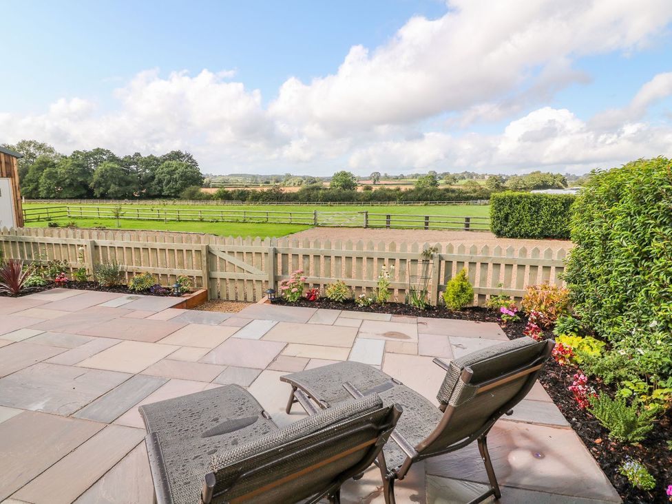 A patio area with chairs and flowers overlooking a lawn at The Croft in Ashbourne
