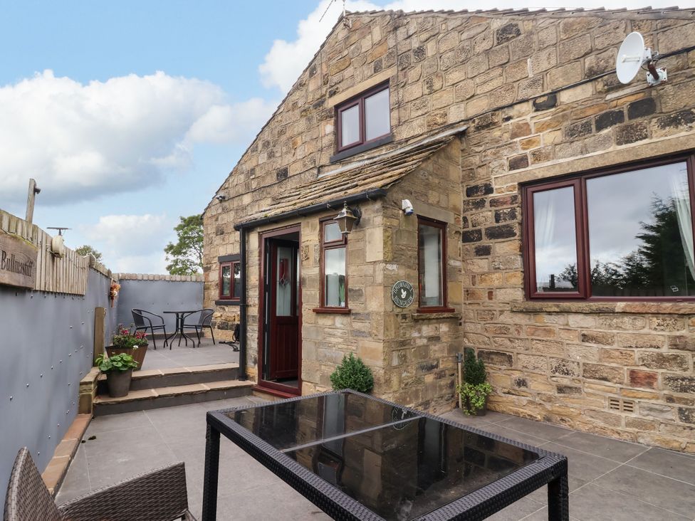 An outdoor area with a stone wall and table with chairs at Brownhill Bungalow West Morton near Riddlesden