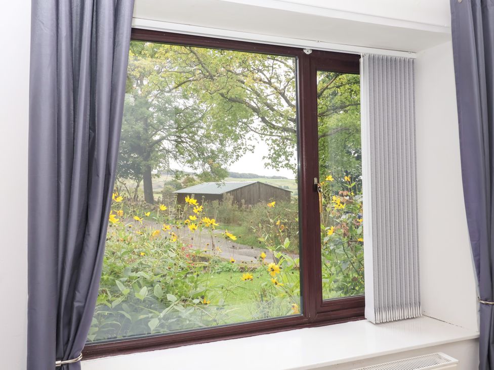 A window with curtains showing flowers and a shed at Brownhill Bungalow near West Morton Riddlesden
