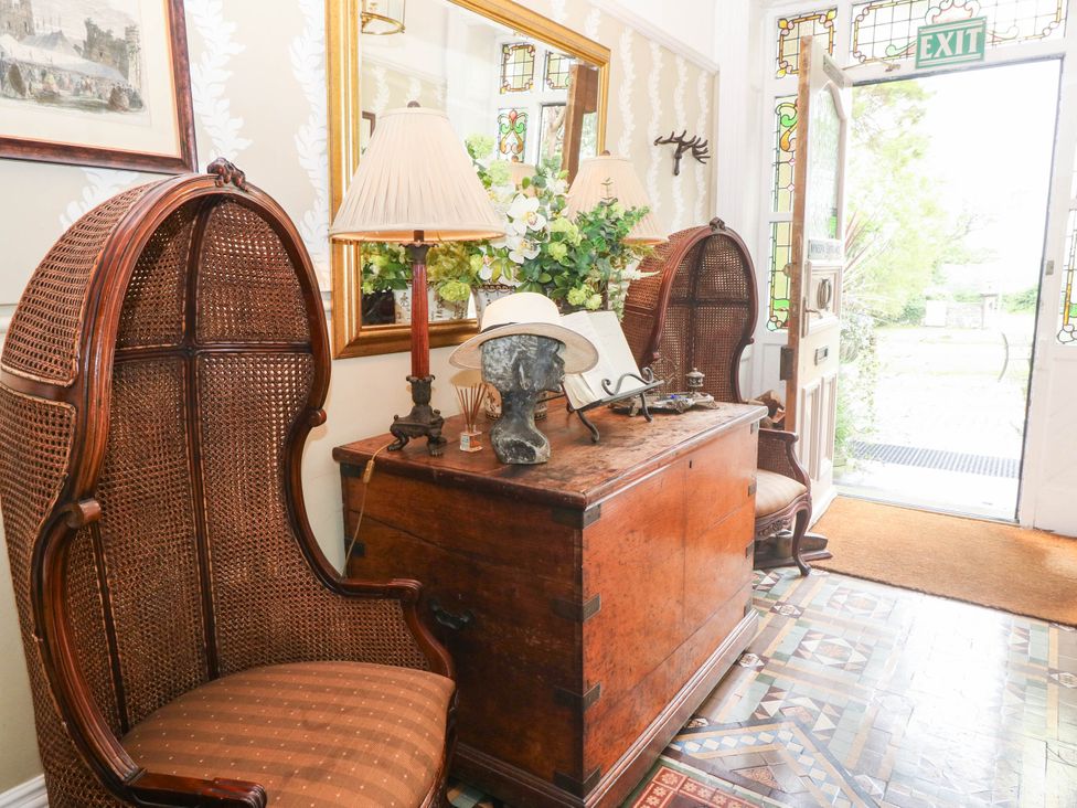 A hallway with two wicker chairs and a wooden chest at Meifod Country House in Caernarfon