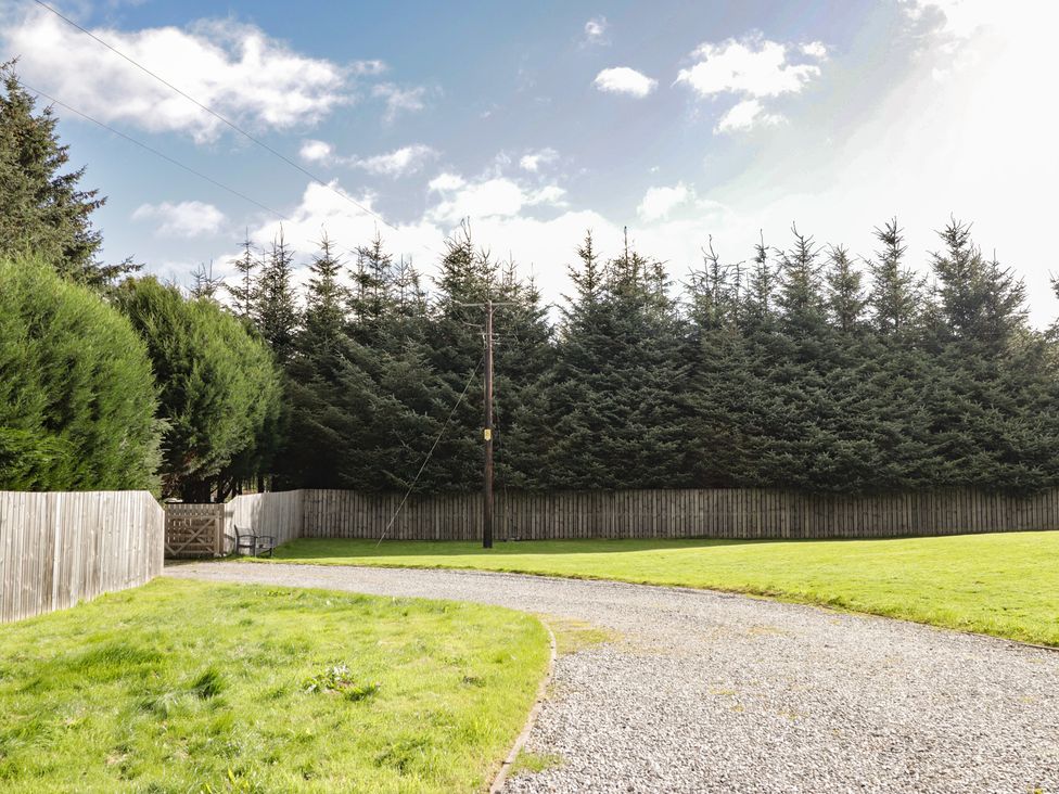 A garden with a gravel driveway and tall trees at Broomfield Hideaway near Inverness