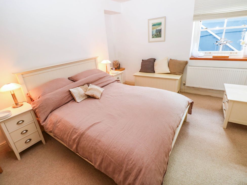 A bedroom with a bed, nightstand, lamp, and window at Basement Apartment in Tenby