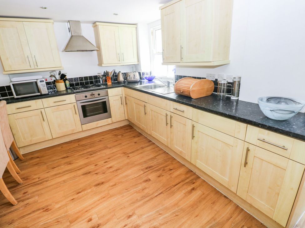 A kitchen with wooden cabinets and appliances at Basement Apartment in Tenby