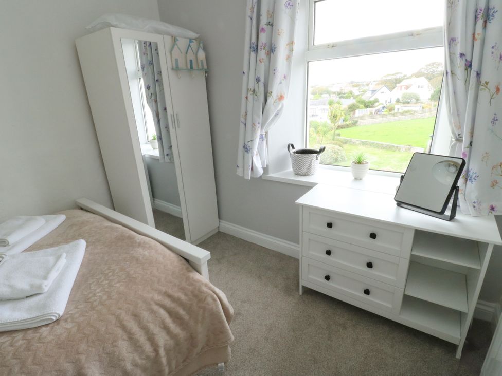 A bedroom with a bed, wardrobe, table, and window at Mor Awelon in Moelfre