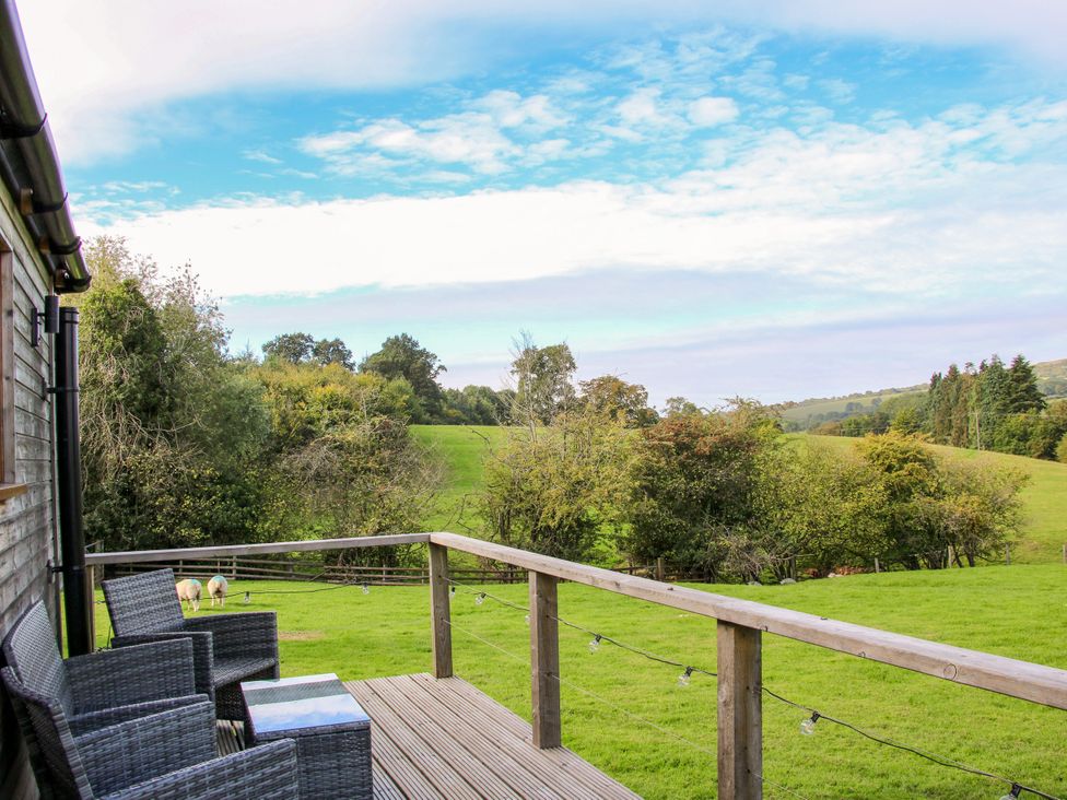 A deck with chairs and a table overlooking grass and trees at Hideaway Hut at Hopton Court Estate near Cleobury Mortimer