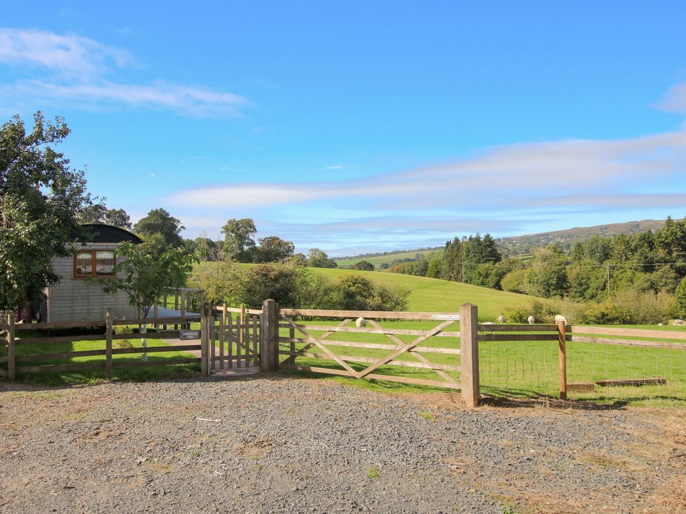A gate opening to a grassy field with a cabin and trees at Hideaway Hut at Hopton Court Estate Hopton Wafers near Cleobury Mortimer