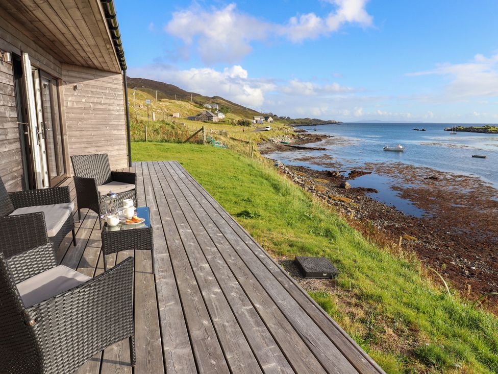 An outdoor patio with chairs and a table overlooking the sea at Holm in Strond near Carminish, Isle Of Harris