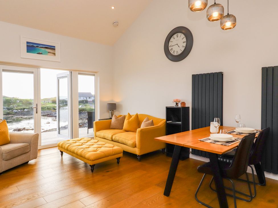 A living room with a yellow sofa and dining table at Holm, Strond near Carminish, Isle Of Harris