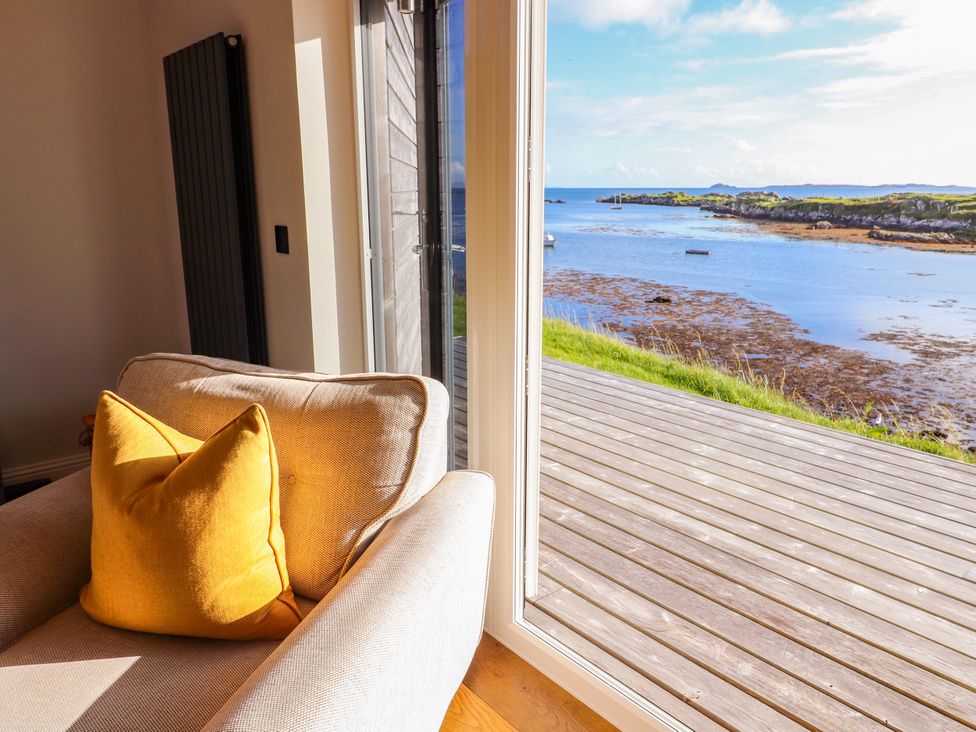 A living room with an armchair and a view of the sea at Holm in Strond near Carminish, Isle Of Harris