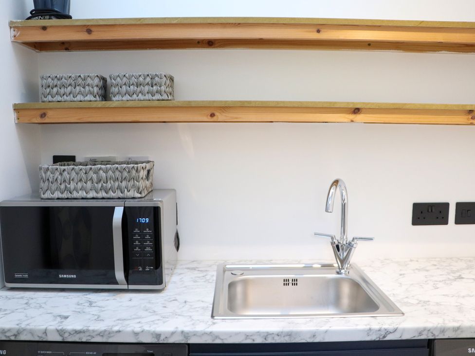 A kitchen with a microwave, sink, and shelves at Holm, Strond near Carminish, Isle Of Harris