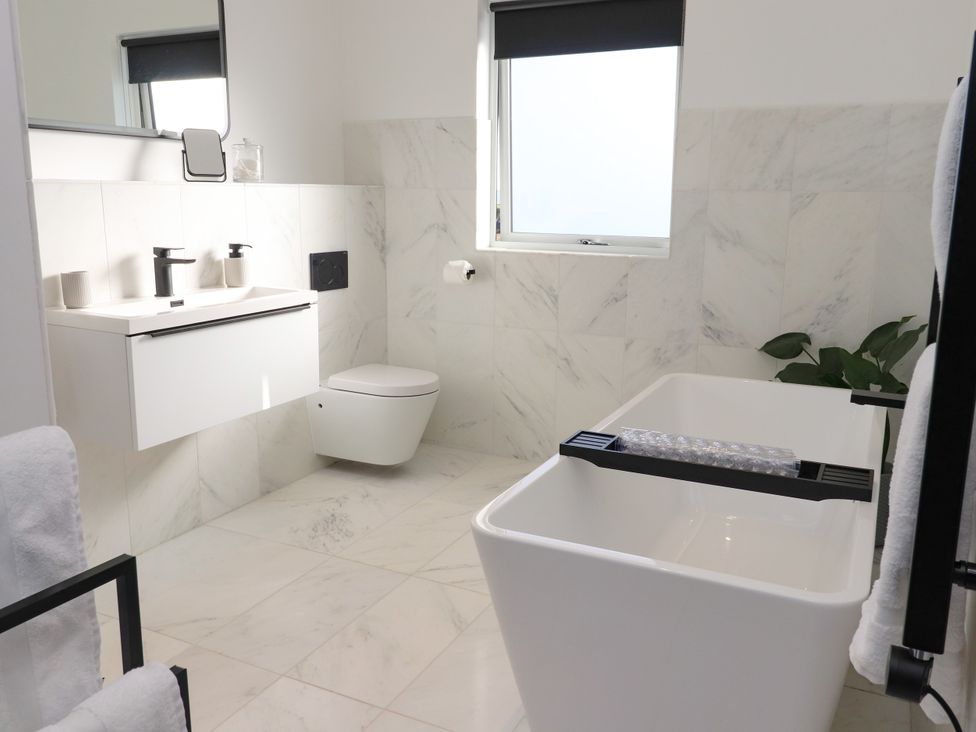 A bathroom with a bathtub, toilet, sink, and mirror at Holm in Strond near Carminish, Isle Of Harris