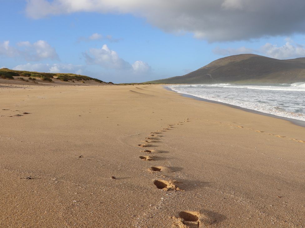A beach with footprints leading towards the ocean at Holm in Leverburgh