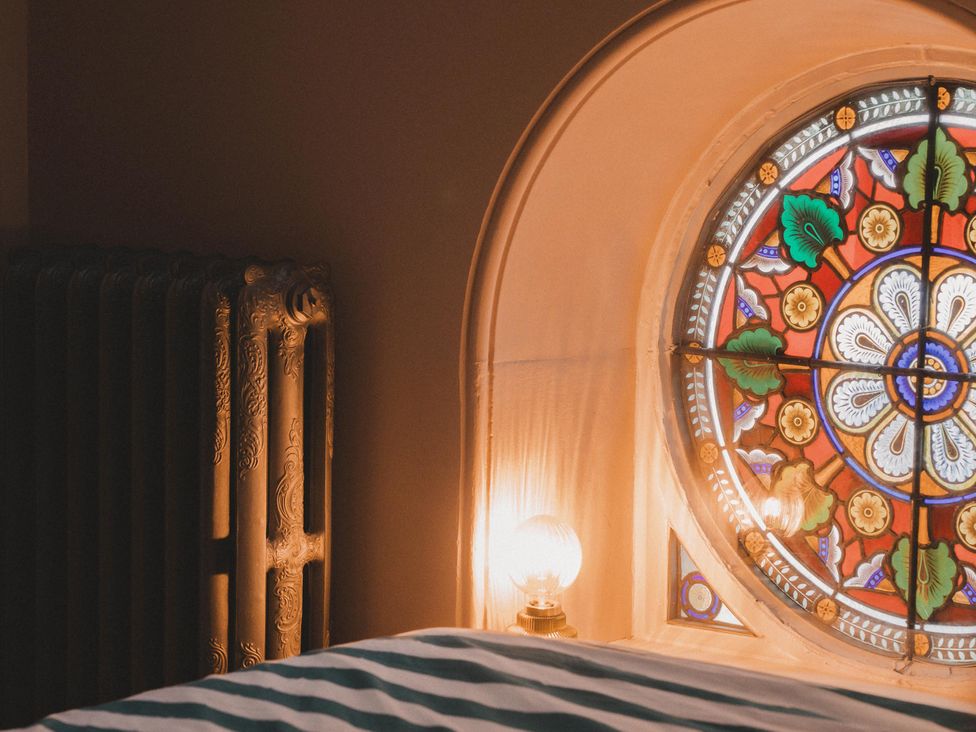 A bedroom with a stained glass window and a radiator at Chapel of Arts in Criccieth