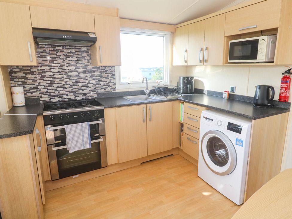 A kitchen with a stove, sink, and washing machine at No.73 Sennen Cove