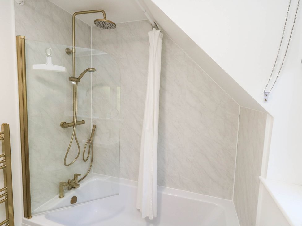 A bathtub with a shower setup at Osmington Cottage Annex