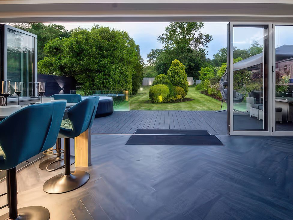 A room with bar stools and a glass door leading to a garden at 19 Hillside Road Northwood, Hertfordshire