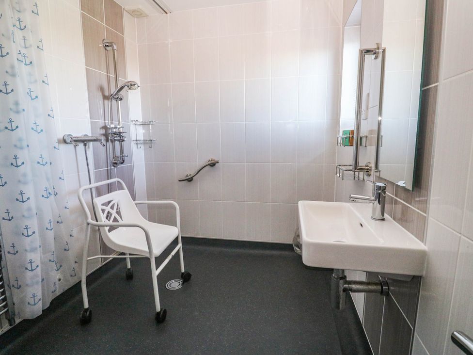 A bathroom with a shower, wash basin and chair at 74 Porthmeor in Redruth