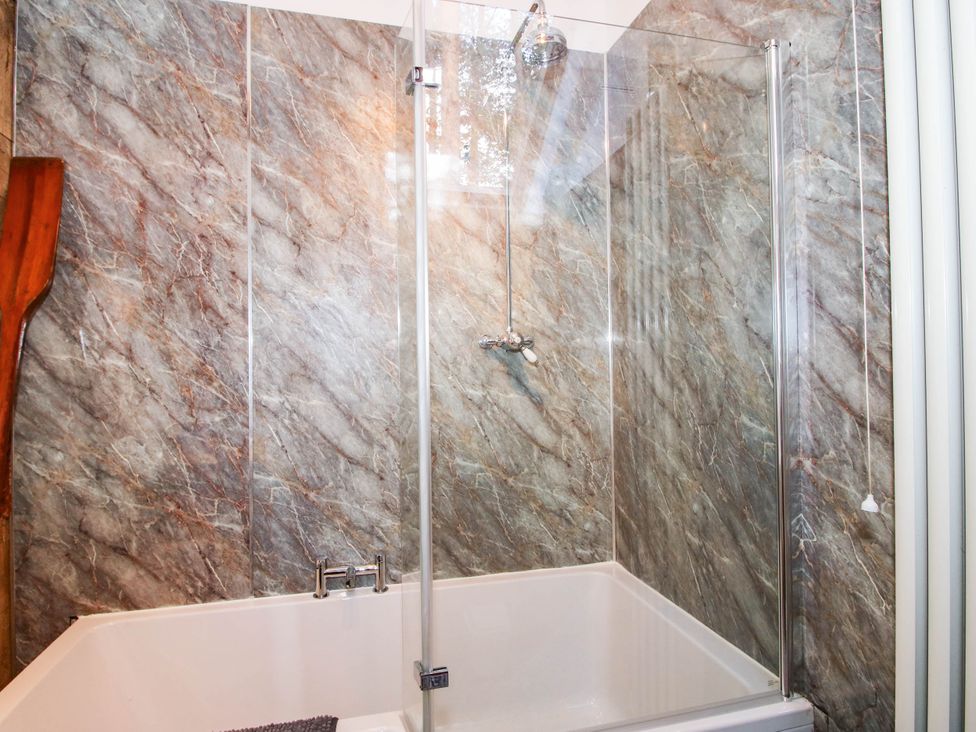 A bathtub with showerhead and glass screen at The Duck House at Hyssington Farm