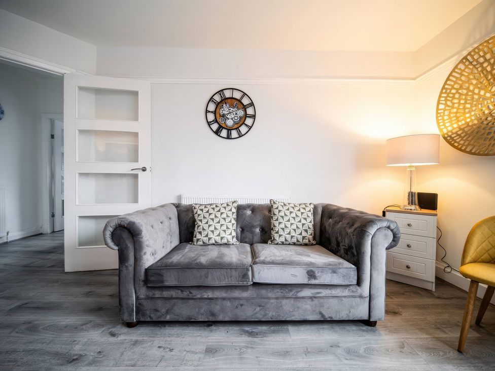A living room with a sofa, clock, and lamp at Flat with Terrace Style Rooftop in Thornton-Cleveleys