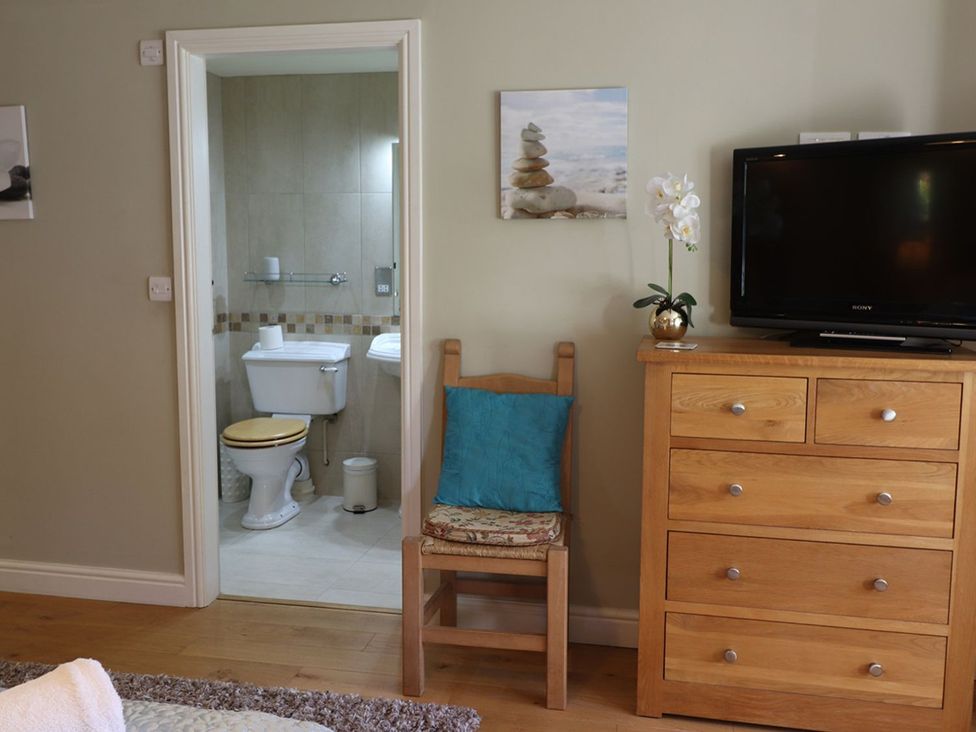 A bedroom with a chair and television and a bathroom doorway at High Beck in Kendal