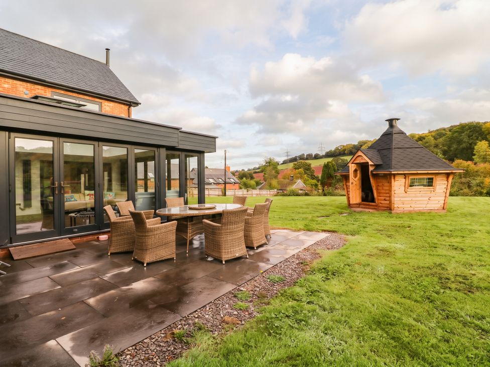 An outdoor area with a table and chairs beside a wooden cabin at Hanbury House in Lea
