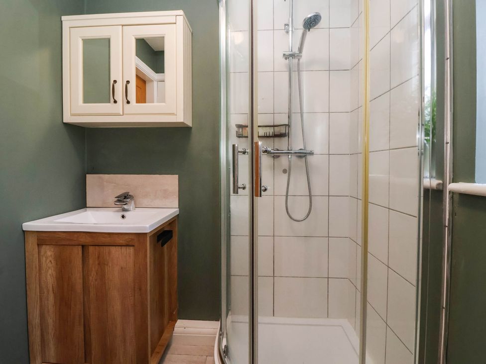 A bathroom with a sink, cabinet, and shower at The Snug 