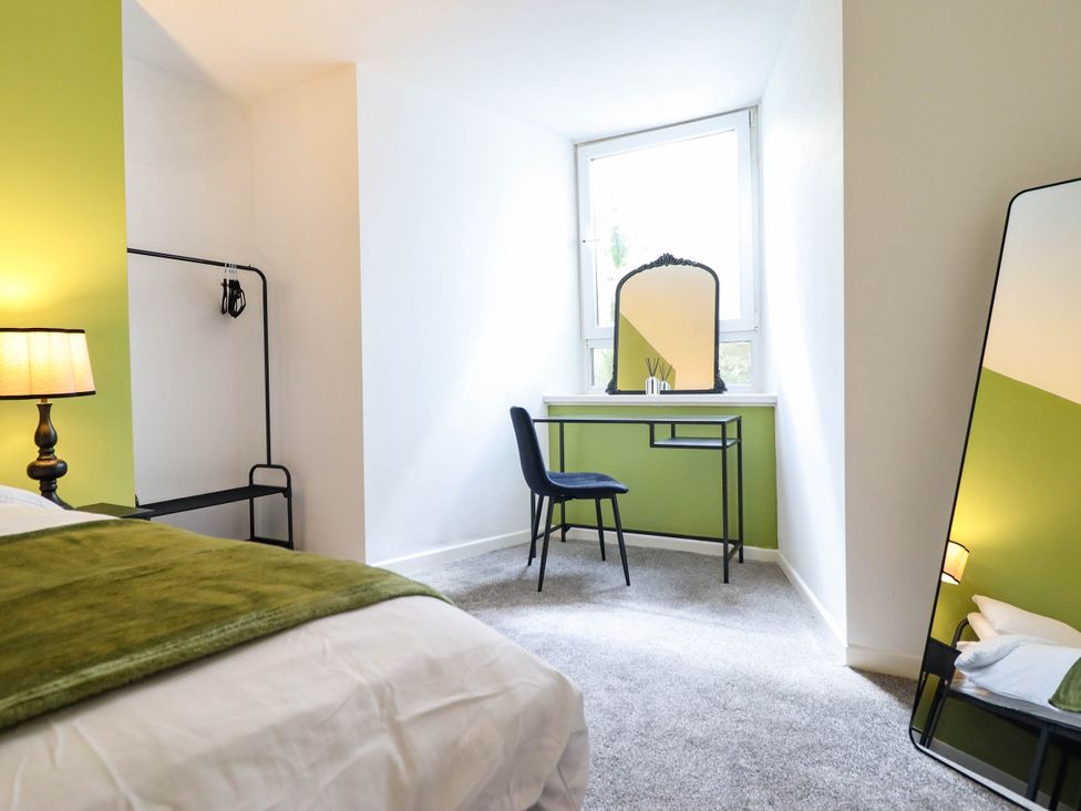 A bedroom with a bed, desk, chair, mirror, and lamp at Flat 1 Greenfields in Barmouth
