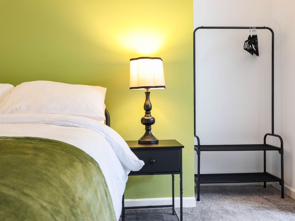 A bedroom with a bed, nightstand, lamp, and clothing rack at Flat 1 Greenfields in Barmouth