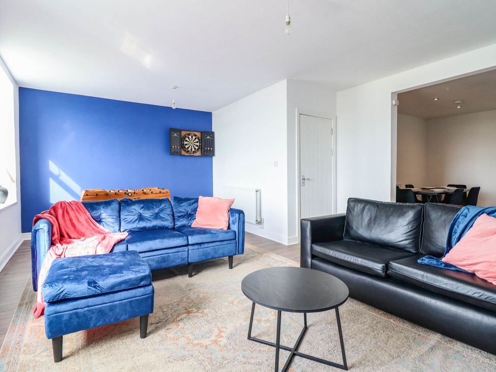 A living room with blue and black sofas and a dartboard at Flat 4 Greenfields Barmouth