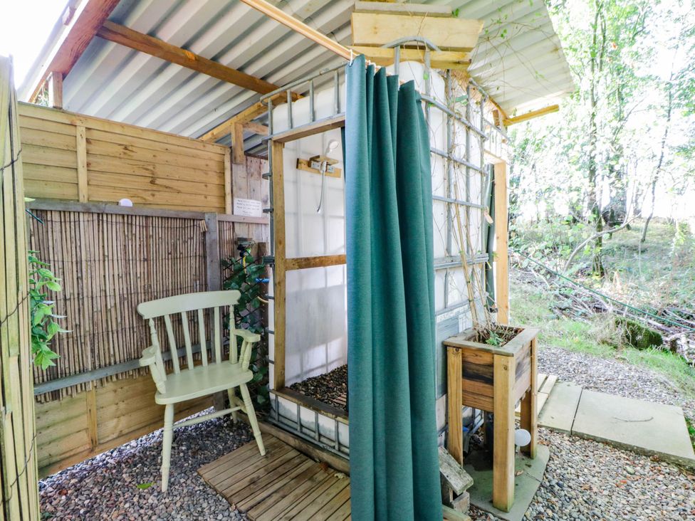 An outdoor shower area with a wooden chair and planter at Bell Tent in Builth Wells
