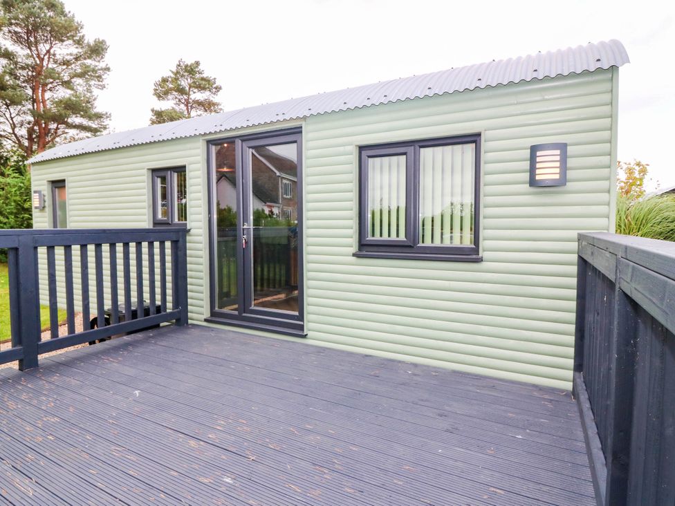 An outdoor view of a cabin with a deck and multiple windows at Calendonia Hut West Mains near Haggerston
