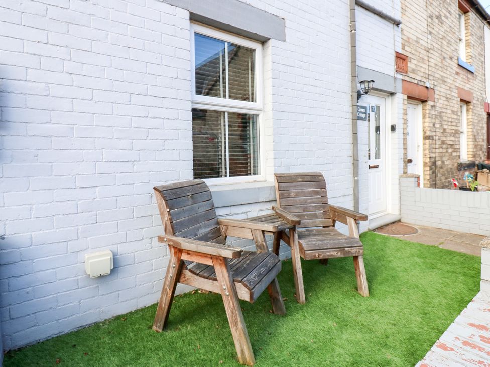 Two wooden chairs and a small table on artificial grass outside Crown Cottage in Appleby-In-Westmorland