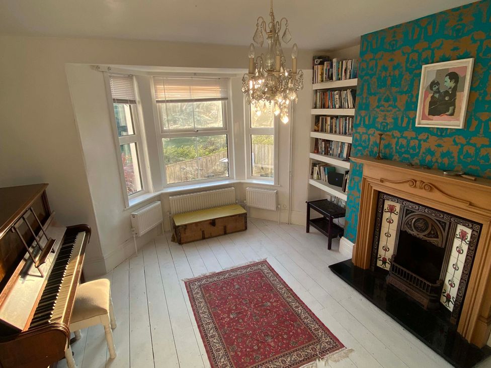 A living room with a piano and bookshelf at Strand House Treknow near Tintagel