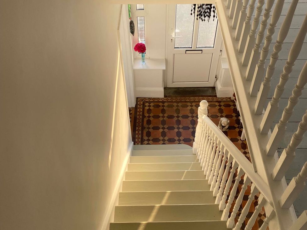 A hallway with stairs and a vase of flowers at Strand House Treknow near Tintagel