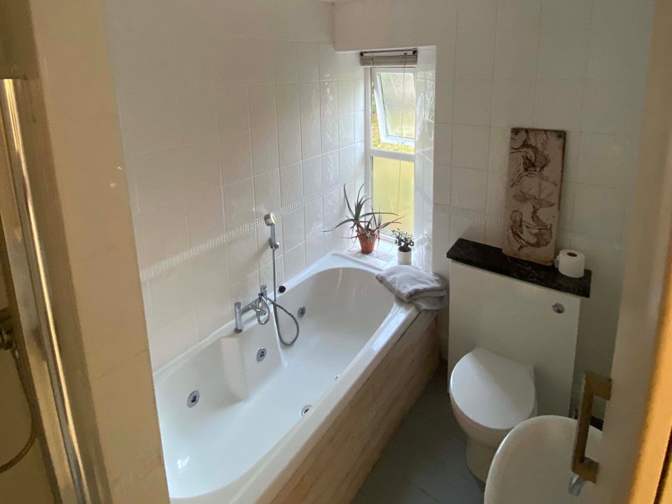 A bathroom with a bathtub, toilet, and window at Strand House Treknow near Tintagel