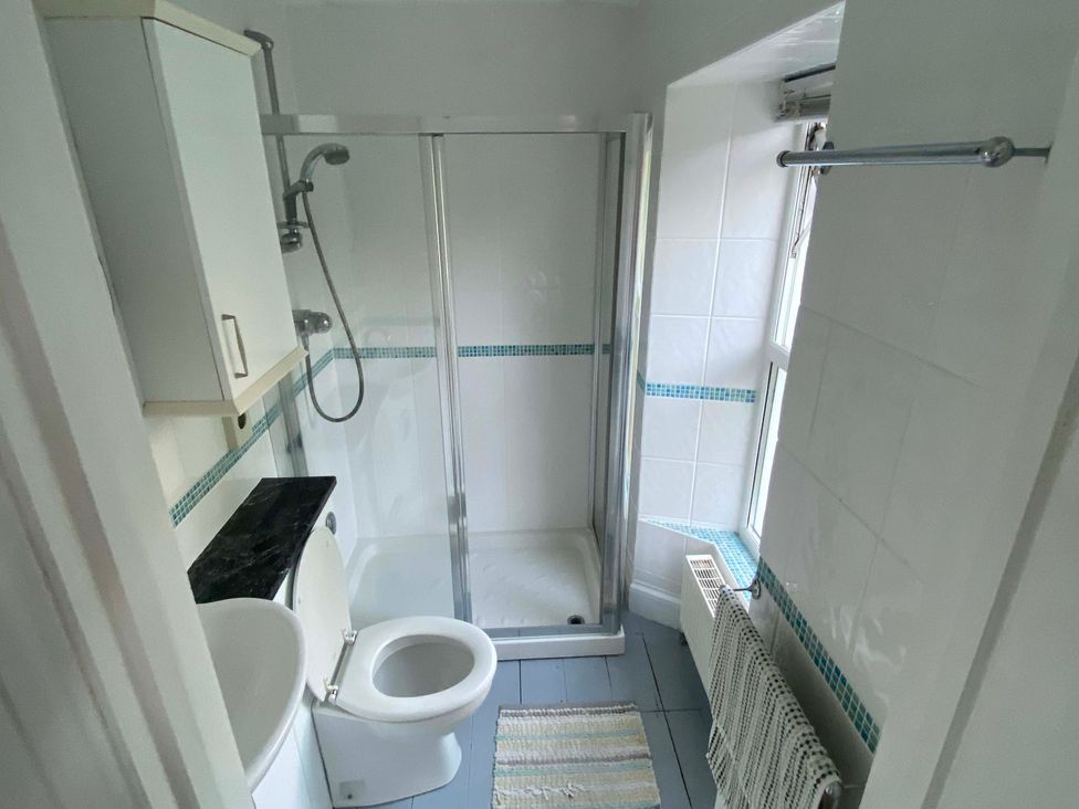 A bathroom with a shower, toilet, sink, and cabinet at Strand House in Treknow near Tintagel